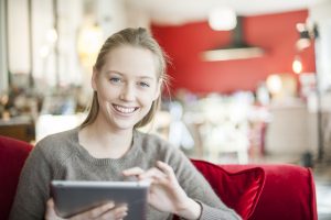 Junge Frau sitzt auf der Couch und benutzt ihr Tablet